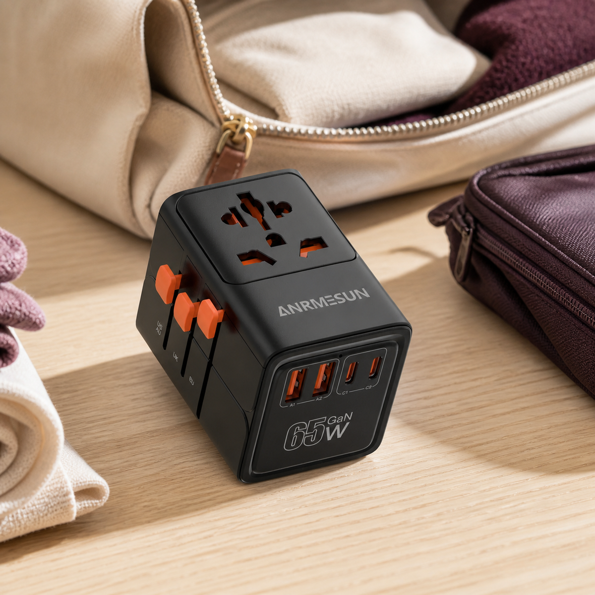 Black travel adapter with orange sliders laid out beside a weekend bag, shown unplugged.